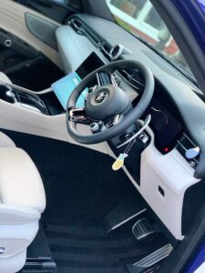 Interior of a modern car featuring a sleek dashboard with a touchscreen panel, steering wheel with the car's logo, white leather seats, and black carpeting. A key fob is inserted into the ignition, and the gear shift is visible between the front seats.