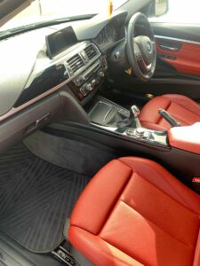 This is an interior view of a car with red leather seats and a black dashboard. The central console features various controls, a gear stick, and an infotainment screen. The steering wheel has buttons, and the car has sporty styling with elegant detailing.