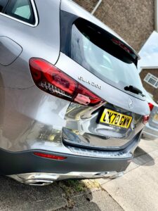 A silver Mercedes-Benz GLA 200 SUV is parked on a street near a brick building. The rear of the vehicle, including its license plate "LX70 GMW," is visible. The sun reflects off the car's polished surface, highlighting its sleek design.